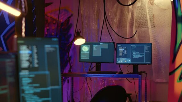 Software interface on computer screen showing programming code used for making malware in empty warehouse with graffiti sprayed on walls. Hacking script running on PC monitors in underground base