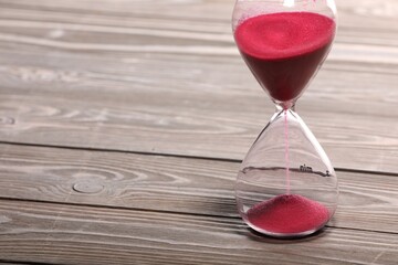 Hourglass with pink flowing sand on wooden table. Space for text