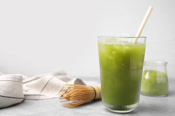 Glass of delicious iced green matcha tea and bamboo whisk on light grey table, space for text