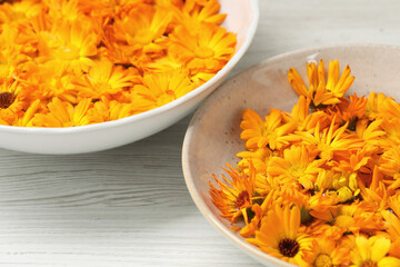 Beautiful calendula flowers in bowls on white wooden table, closeup