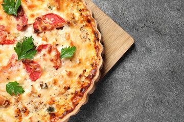 Tasty quiche with tomatoes, parsley and cheese on grey textured table, top view. Space for text