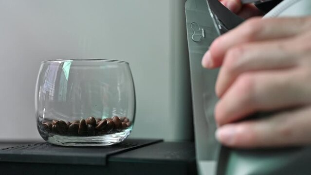Barista holding a tablespoon roasted coffee beans and adding coffee beans into a glass cup for measuring weight.
