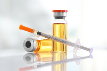 Glass vials and syringe with orange medication on white table, closeup