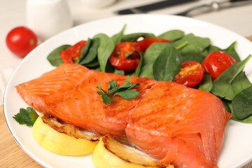 Tasty grilled salmon with basil, tomatoes and lemon on table, closeup