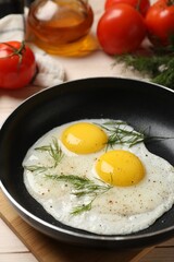 Frying pan with tasty cooked eggs, dill and other products on light wooden table, closeup
