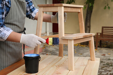 Man varnishing wooden step stool at table outdoors, closeup