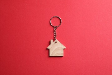 Wooden keychain in shape of house on red background, top view