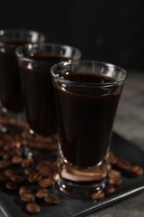 Shot glasses with coffee liqueur and beans on grey table, closeup