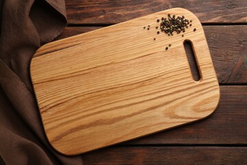 New cutting board and peppercorns on wooden table, flat lay