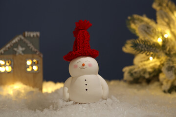 Cute decorative snowman, hut and Christmas tree on artificial snow against dark background