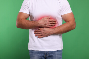 Man suffering from stomach pain on green background, closeup