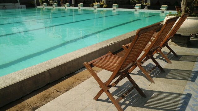 wooden relax chairs on floor near swimming pool in simple design.