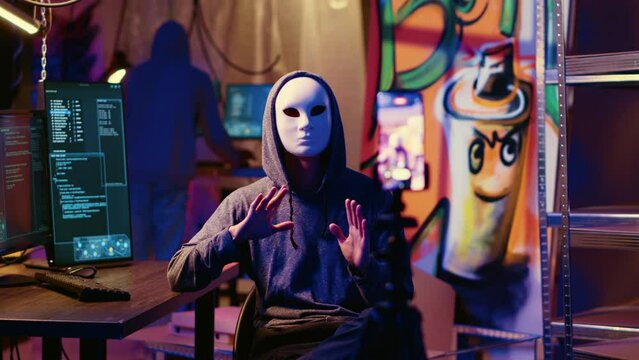 Masked hackers filming ransom video in hidden underground base, threatening to release stolen data publicly if payout demands are not met. Rogue programmers using phone to record blackmail footage
