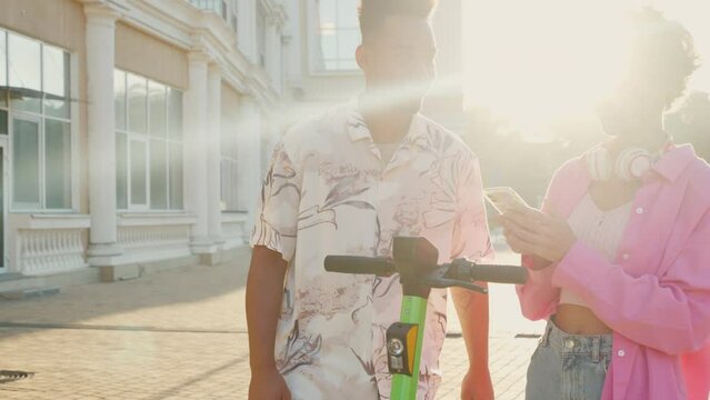 Multiracial friends using smartphone app to unlock shared electric push scooter for riding in the city.