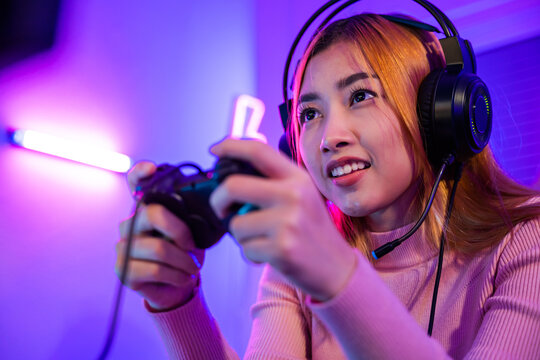 You win. Gamer using joystick controller plays online video game with computer neon lights very determined, woman wear gaming headphones playing live stream esports games console at home
