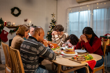 Multi-ethnic big family saying a prayer before having Christmas dinner. 