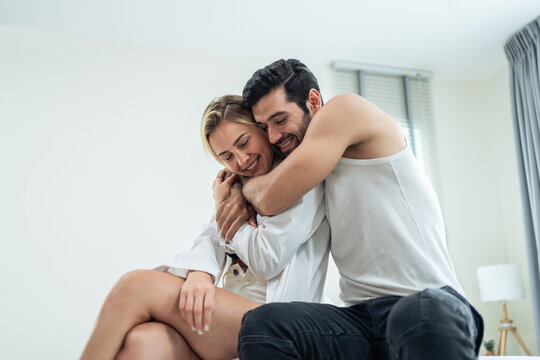 Caucasian young couple sitting on bed and hugging each other with love. 