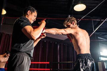 Fototapeta na wymiar Asian fitness trainer support Caucasian sportsman doing boxing in gym.