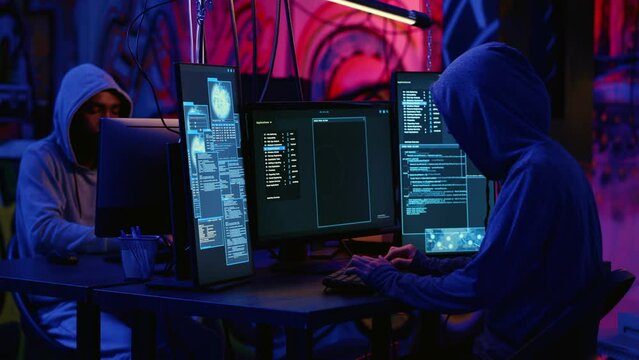 African american hacker and asian colleague working together in hidden place with graffiti walls, deploying malware on unsecured computers to steal sensitive data from unaware users online