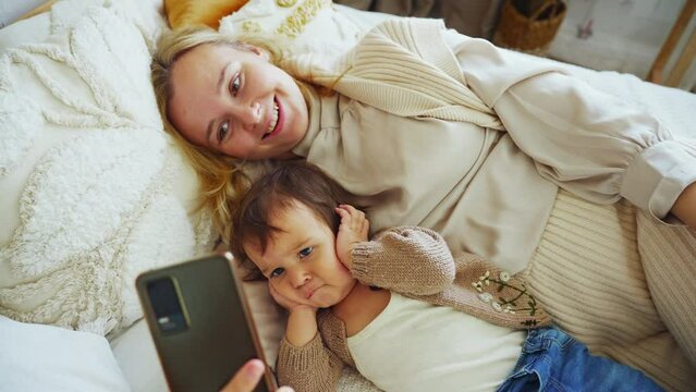 Mother taking selfie with baby boy using mobile phone. 