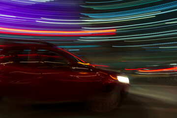 motion photo of red car moving through traffic at night 