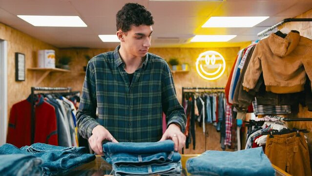 Male sales assistant sorting stock of denim jeans in pop up fashion or clothes store - shot in slow motion
