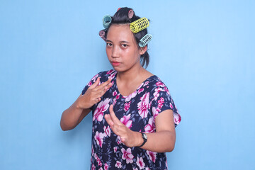 Funny Asian woman with hair curlers rollers on head standing in martial arts pose isolated on blue...