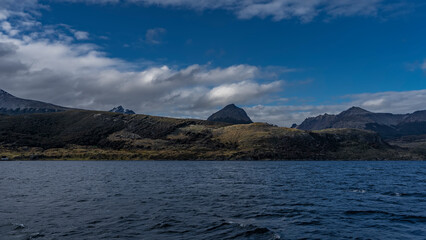 Coastal mountains and hills against a  blue sky and clouds. In the foreground is the surface of the Beagle Channel with ripples on the water. Argentina. The Andes. Tierra del Fuego Archipelago