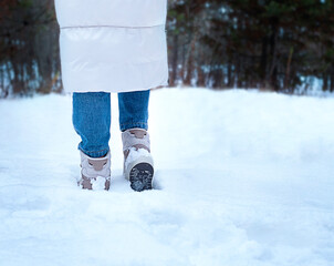 Woman walking in winter forest, closeup of legs and boots.
