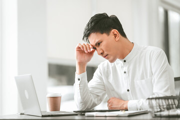 Asian male people concerned person in white shirt looks at laptop, possibly stressed, hand on their forehead. middle age businessman