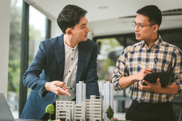 Two middle-aged Asian people businessmen, one holding wind turbine model, discussing over model...