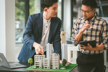 Two middle-aged Asian people businessmen, one holding wind turbine model, discussing over model...