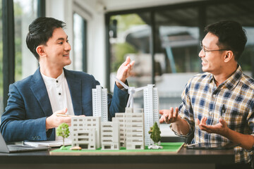 Two middle-aged Asian people businessmen, one holding wind turbine model, discussing over model...