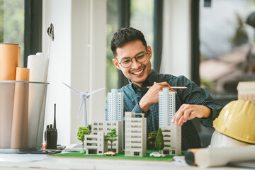 Asian people joyful person businessman engineer holding building model with wind turbines, representing clean energy city with low air pollution, surrounded by more models.
