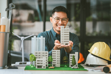 Asian people joyful person businessman engineer holding building model with wind turbines, representing clean energy city with low air pollution, surrounded by more models.