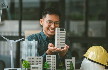 Asian people joyful person businessman engineer holding building model with wind turbines,...