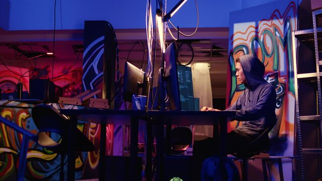 Hacking group leader in neon lit room teaching new member how to write malware lines of code on computer that can get past security systems. Script kiddie learning how to make hacking program