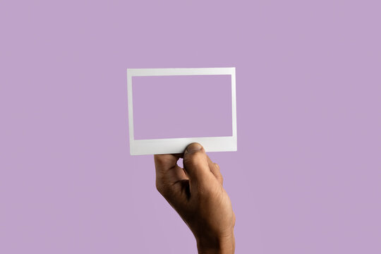 black male hand holding photo frame on isolated on light purple background