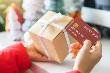 woman's hands holding a gift box and red credit cards against by the festive scene of a beautiful...