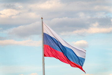 Russian tricolor flag waving in the wind against a blue sky.
