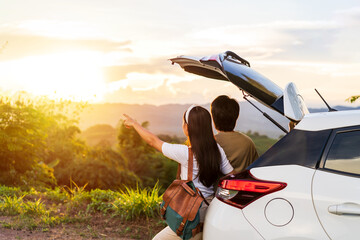 Young couple traveler with car watching a beautiful sunrise over the mountain while traveling road...