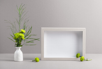 A bouquet of small green chrysanthemums in a white vase and a photo frame on a gray background. Women's workplace, mockup.