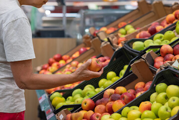 Portrait of senior caucasian woman buying fresh organic vegetables and fruit at market place and holding bag full of healthy food.