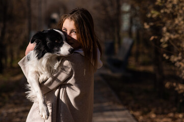 Caucasian woman holding a border collie in her arms while walking in the autumn park. Portrait of a girl with a dog.