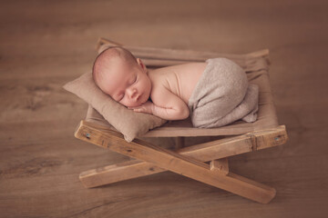 Newborn boy in a suit sleeps on a small chaise lounge