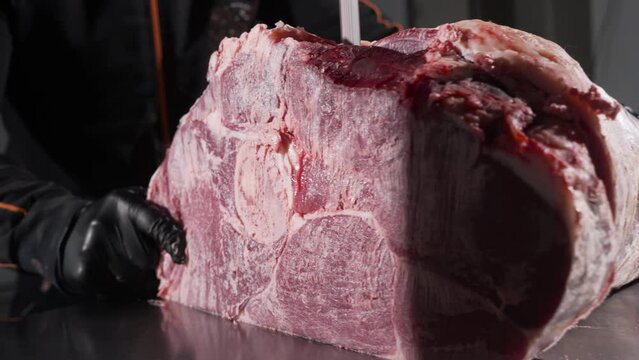 A man holds a raw cow's leg, slicing it into steaks with a band saw.