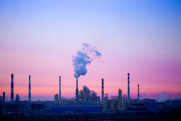 Working oil refinery. Smoke from the factory chimney. Ecological pollution. Air emissions polluting the city. Industrial waste is hazardous to health. A large working factory in the smog at sunset. - obrazy, fototapety, plakaty