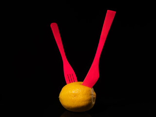 Composition with lemon, knife and fork on a black background