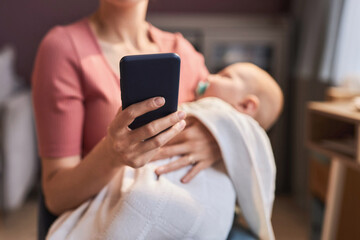 Close up of mother holding smartphone in hand while rocking fussy baby to sleep, copy space