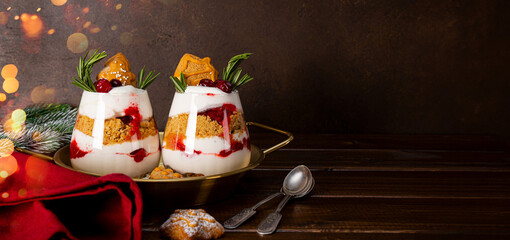 Two glasses of Christmas dessert with gingerbread cookies, whipped cream and cranberries on dark background, web banner with copyspace for text